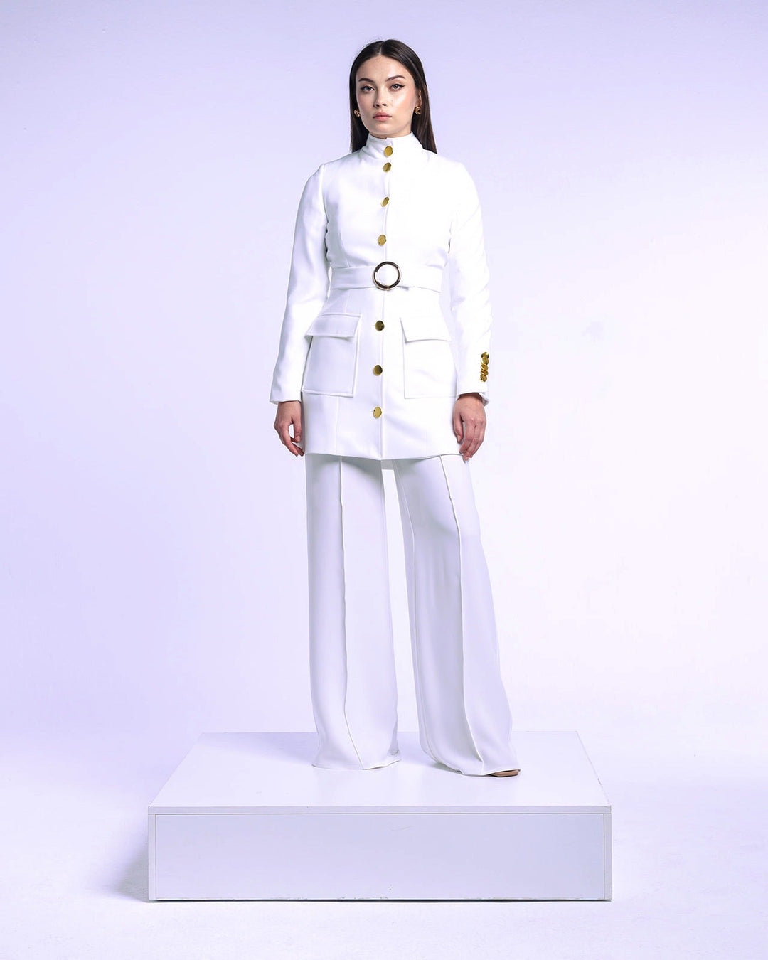 Woman wearing an elegant white tailored suit with gold buttons and wide-leg pants on a platform