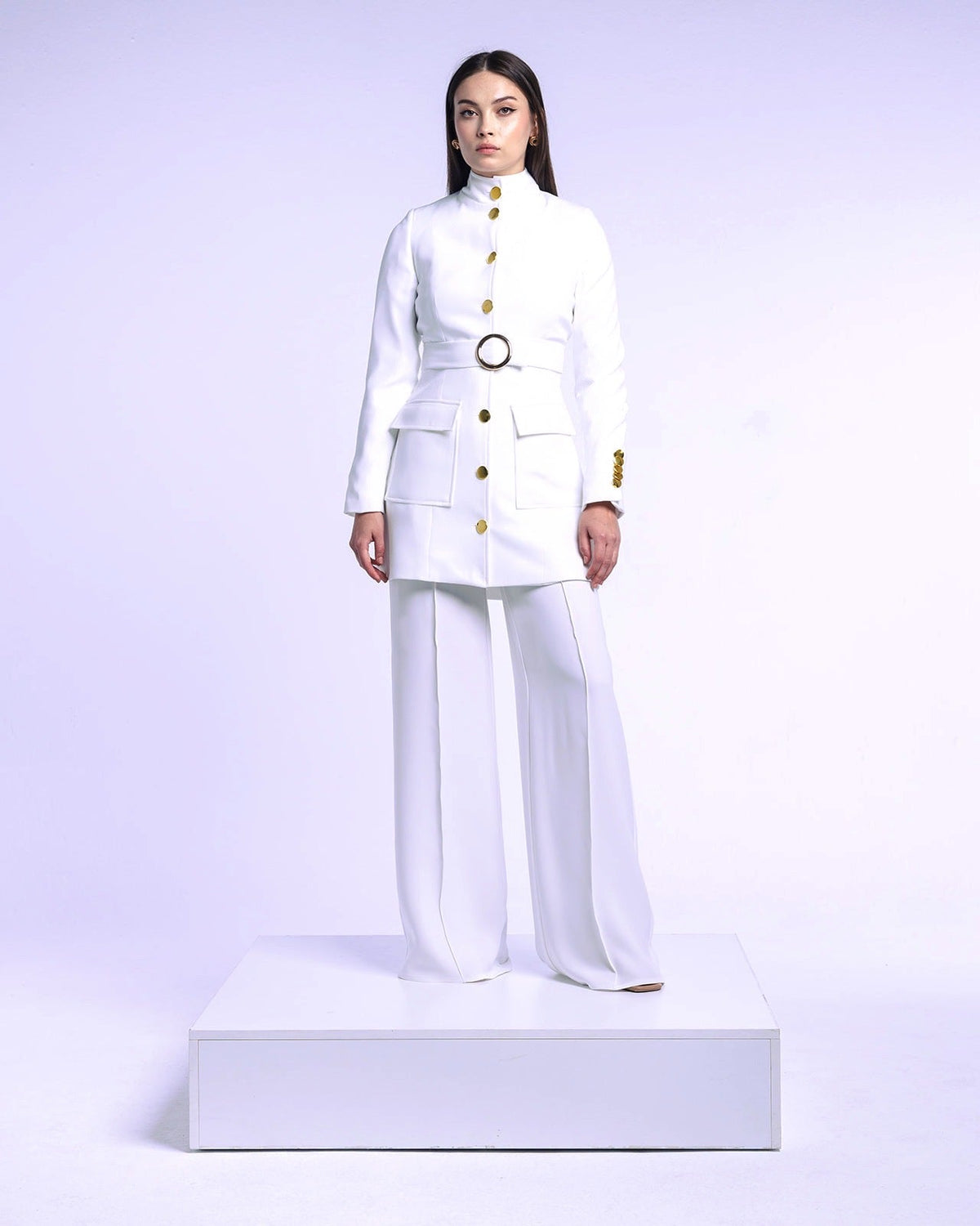 Woman wearing an elegant white tailored suit with gold buttons and wide-leg pants on a platform