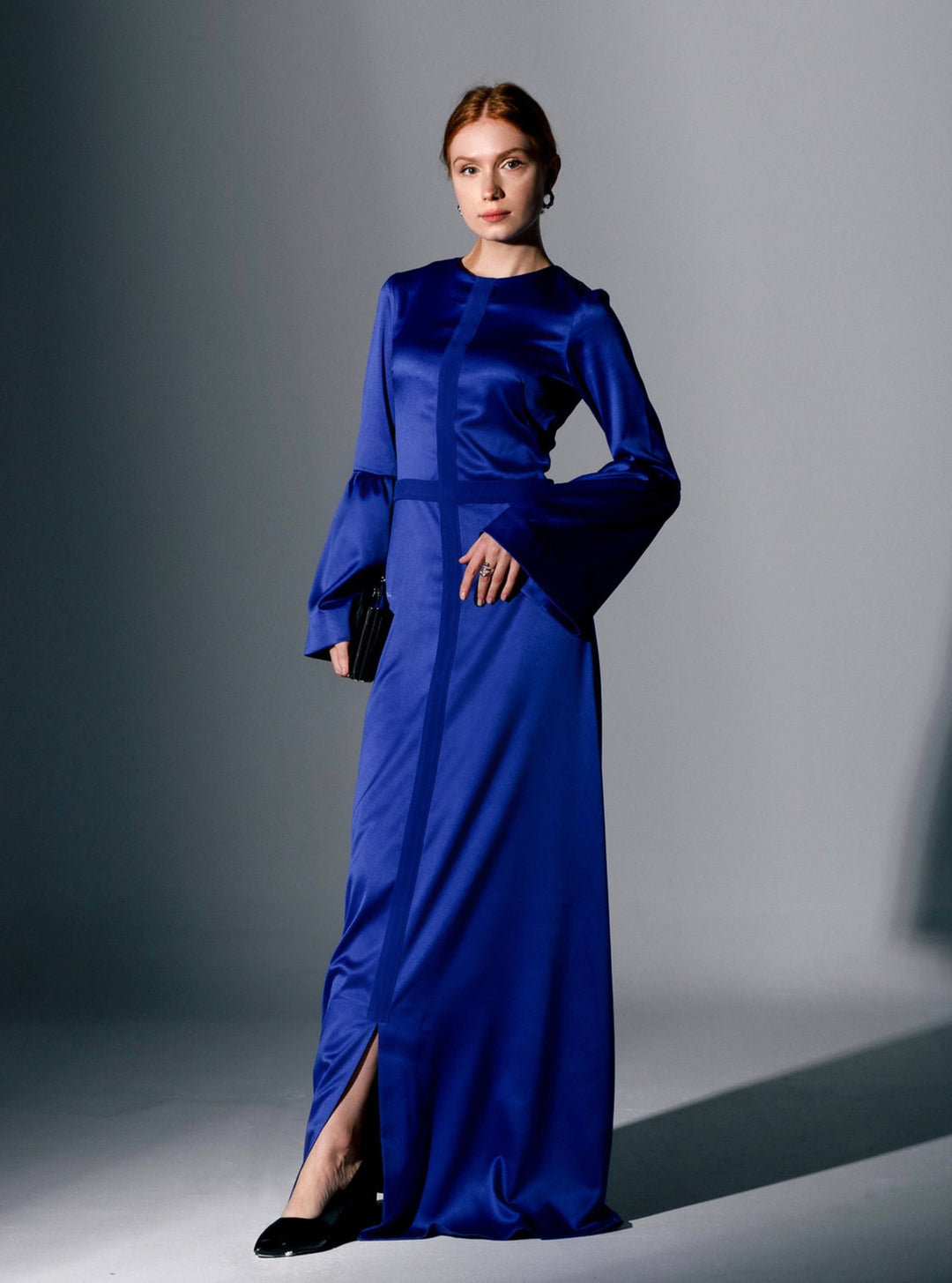 Elegant woman in a royal blue satin maxi dress with bell sleeves and front slit, studio setting