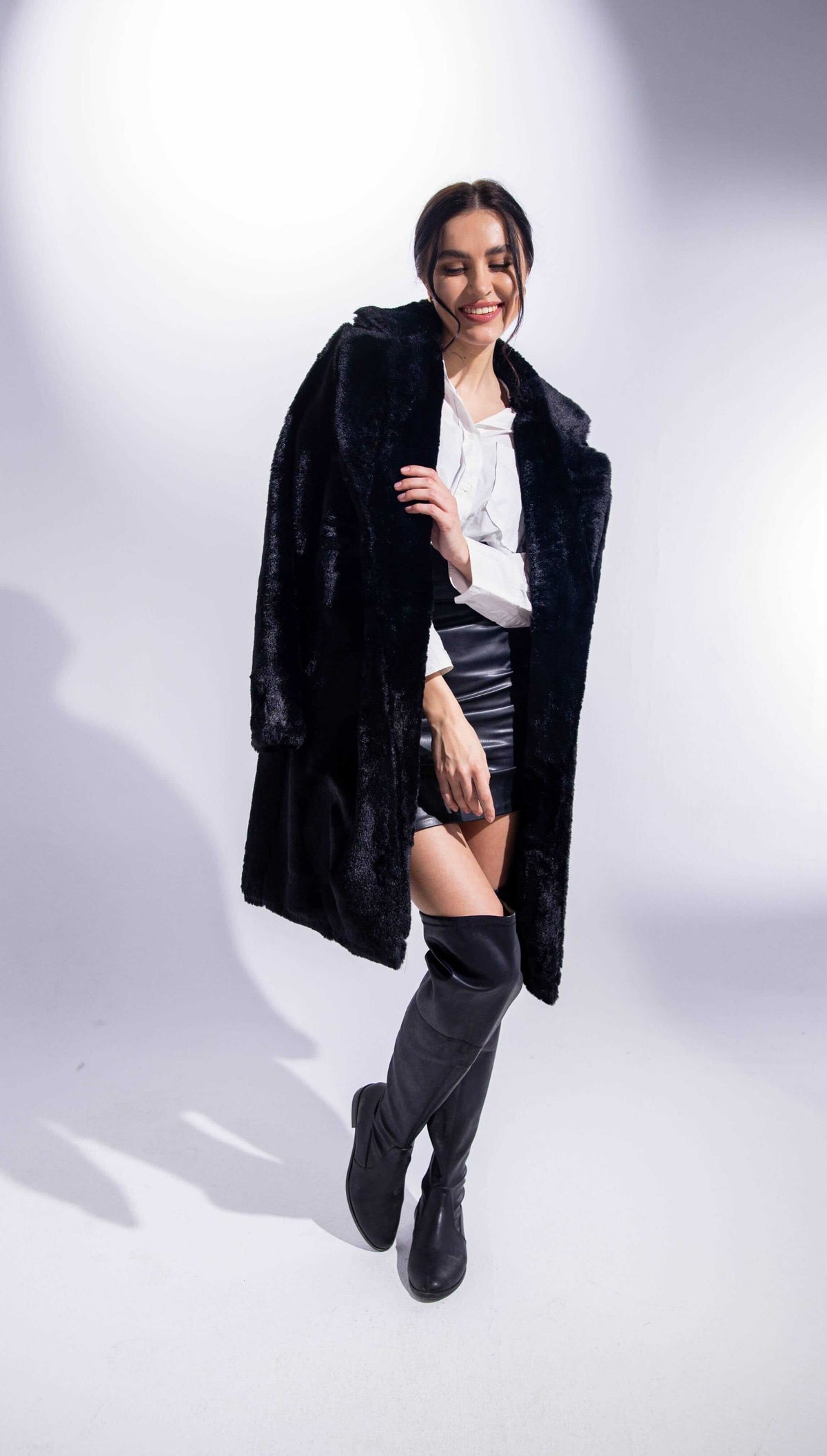 Woman in black faux fur coat, white blouse, black mini skirt, and knee-high boots