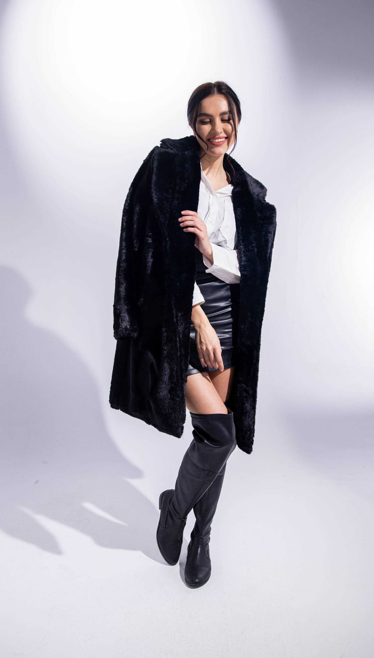 Woman in black faux fur coat, white blouse, black mini skirt, and knee-high boots