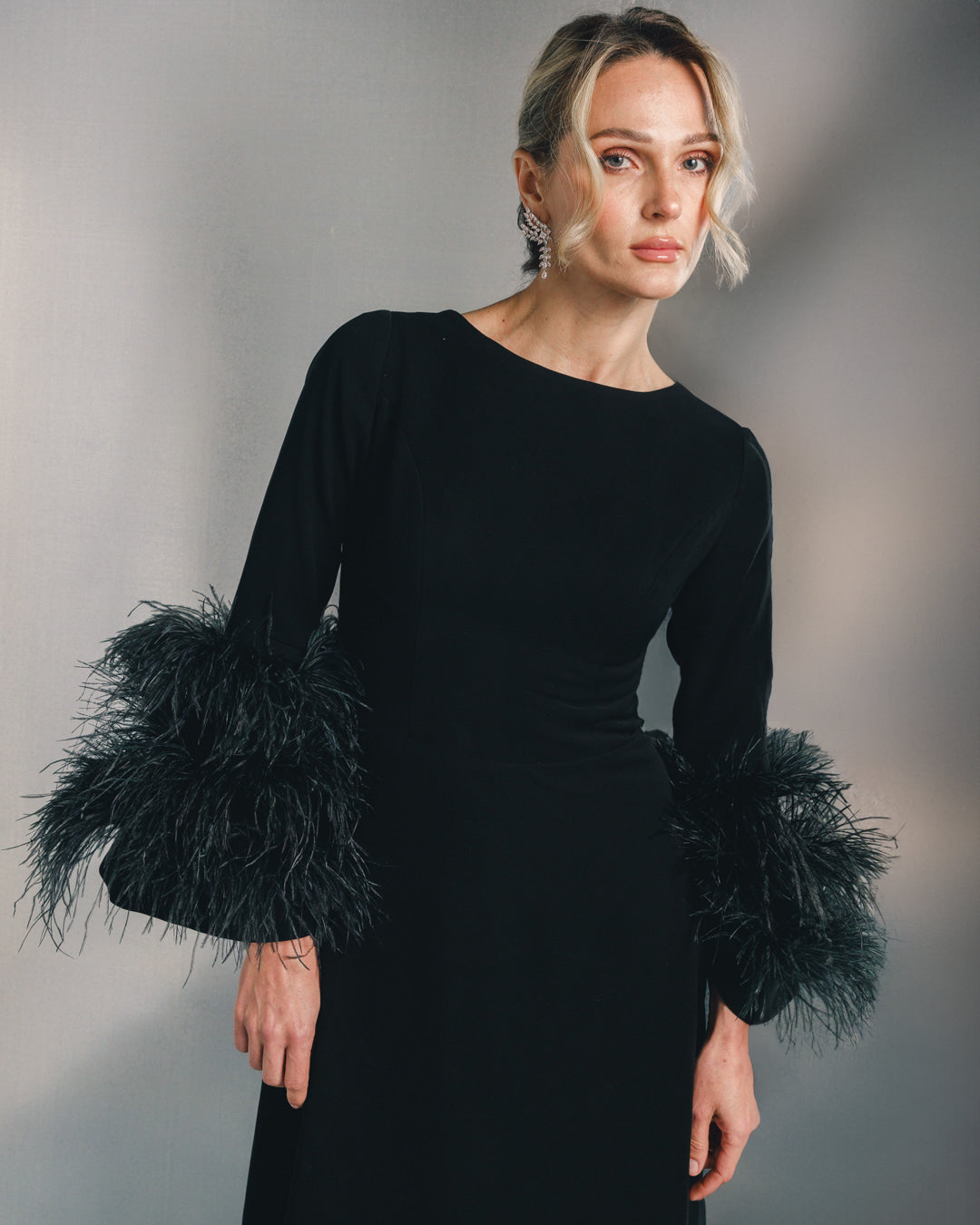 Woman in elegant black dress with feathered sleeves and statement earrings