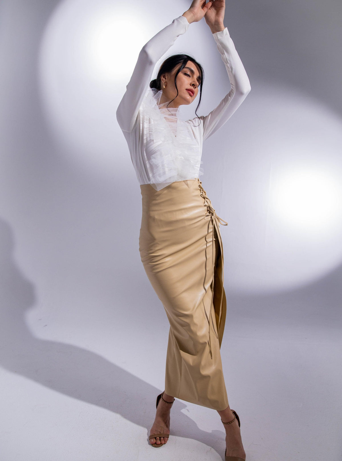 Woman modeling a white ruffle blouse and beige high-waist slit skirt in studio