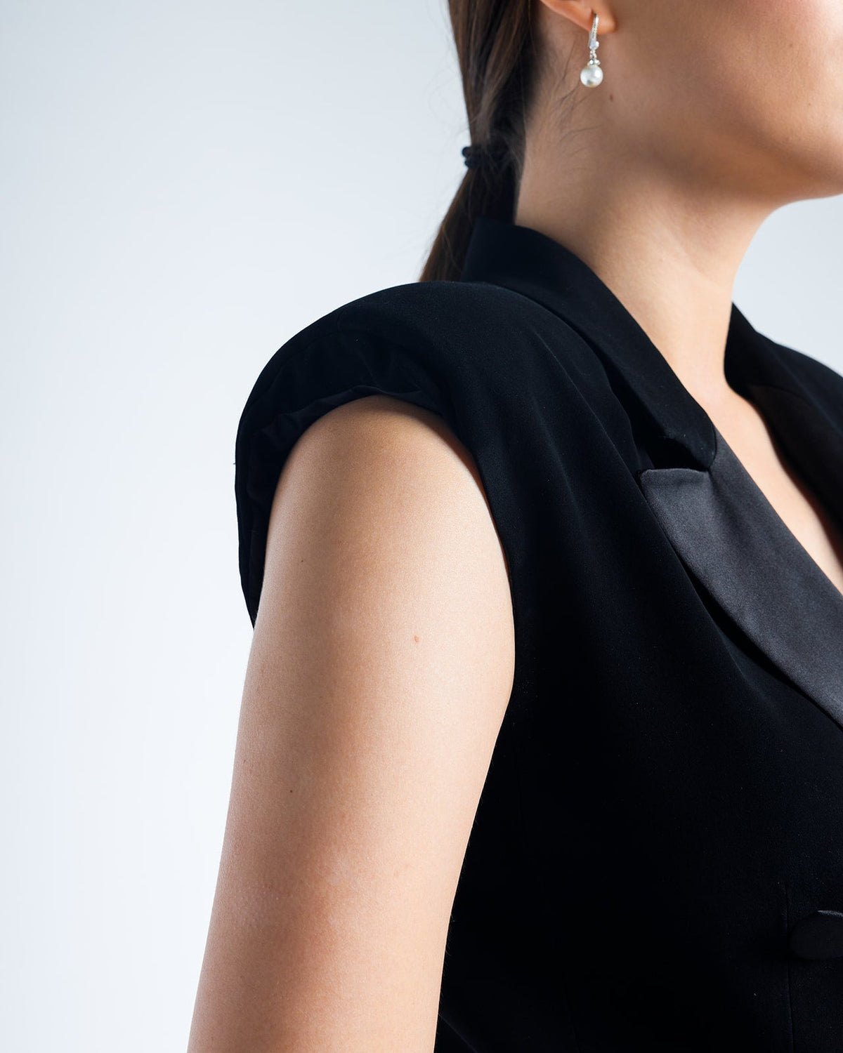 Woman in elegant black sleeveless suit jacket with pearl drop earring
