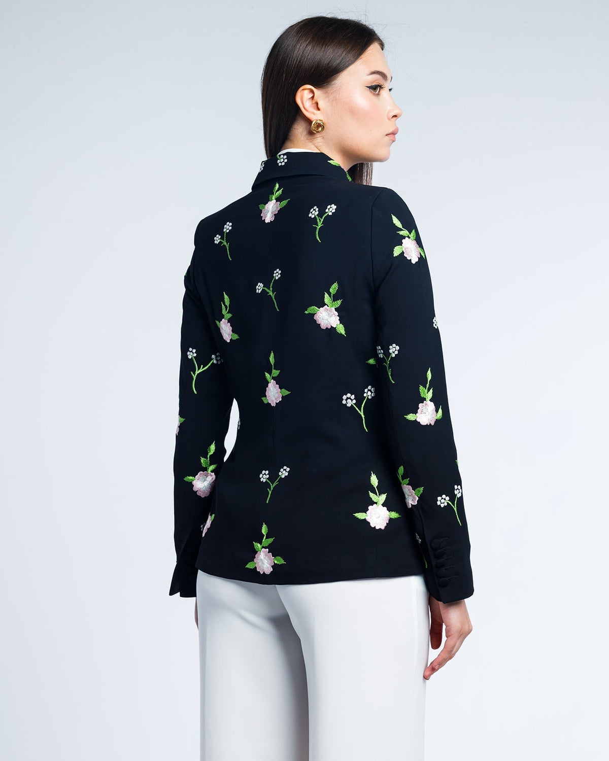 Woman wearing black floral embroidered blazer with white trousers, back view