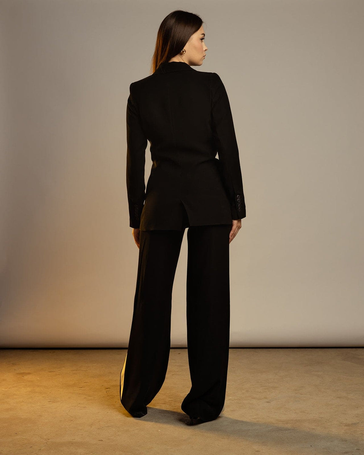 Woman in black tailored suit with wide-leg pants, back view, standing in minimal studio