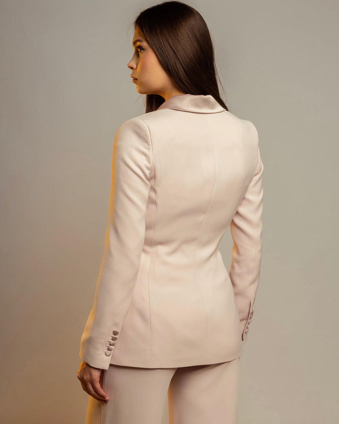 Woman wearing a cream rose tailored blazer suit, viewed from the back, studio lighting