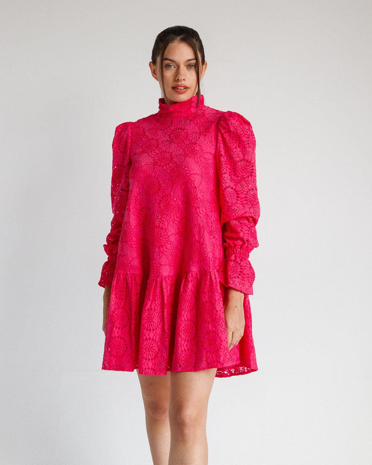 Woman wearing a bright fuchsia lace mini dress with long puff sleeves and high neck
