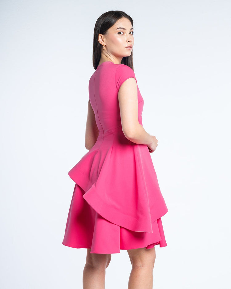 Woman wearing a fuchsia pink short-sleeve layered dress with ruffle detail, posing on white background