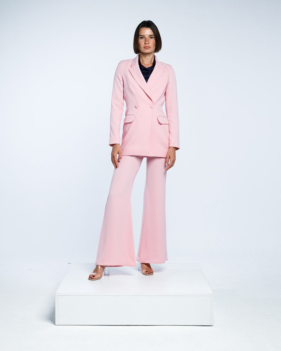 Woman wearing elegant light pink pantsuit with flared trousers and blazer, studio background
