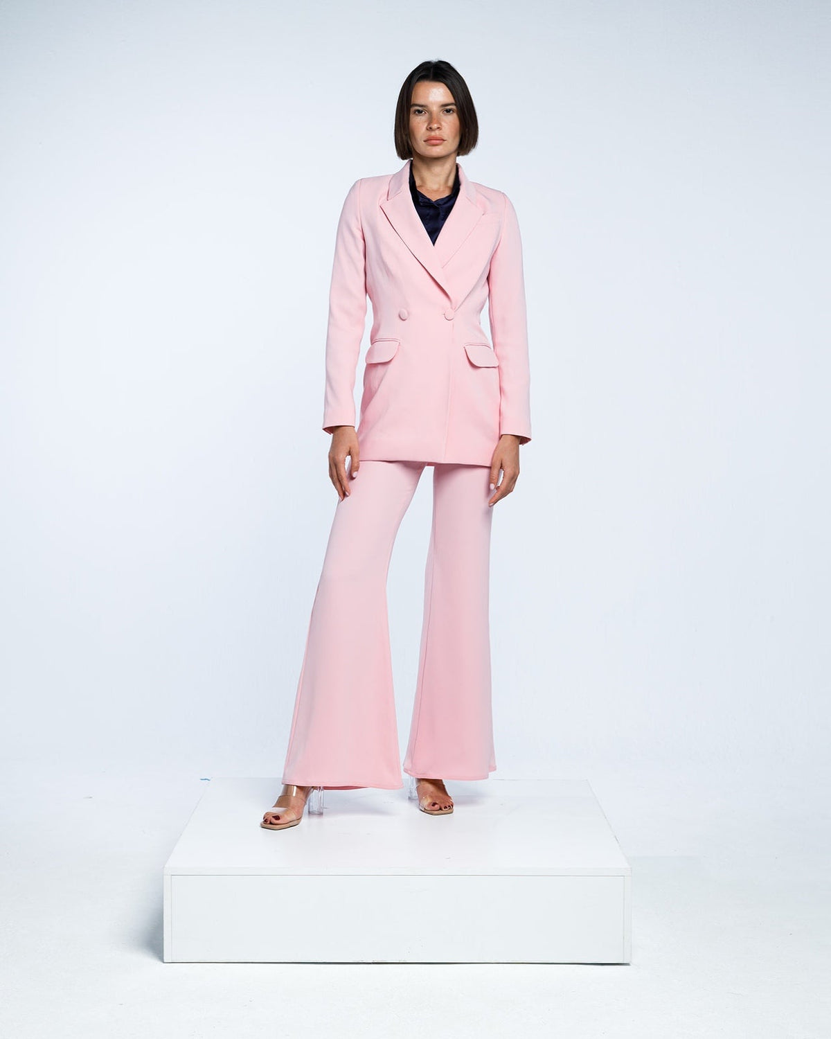 Woman wearing elegant light pink pantsuit with flared trousers and blazer, studio background