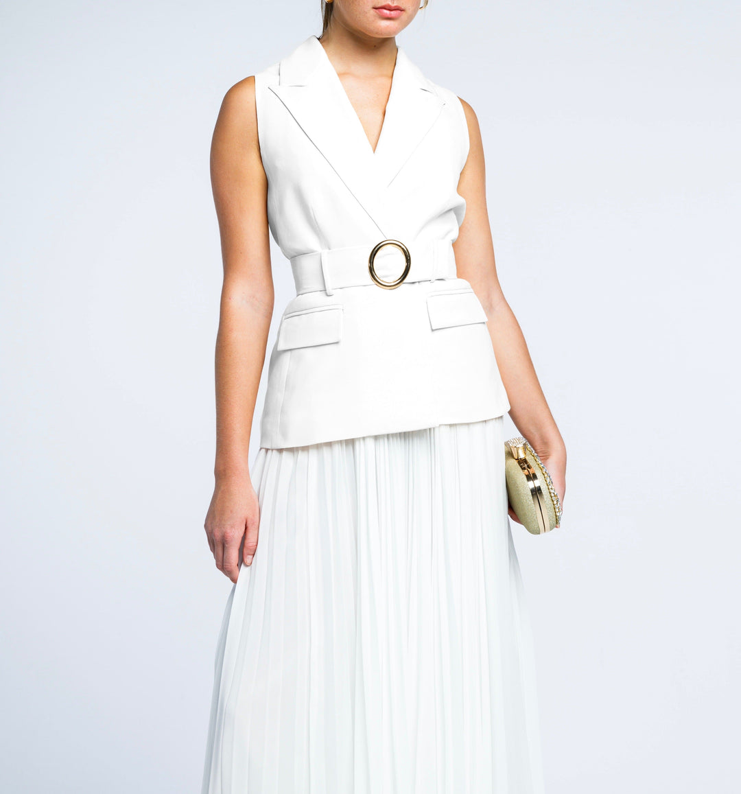 Woman wearing sleeveless white belted blazer and pleated maxi skirt, holding clutch
