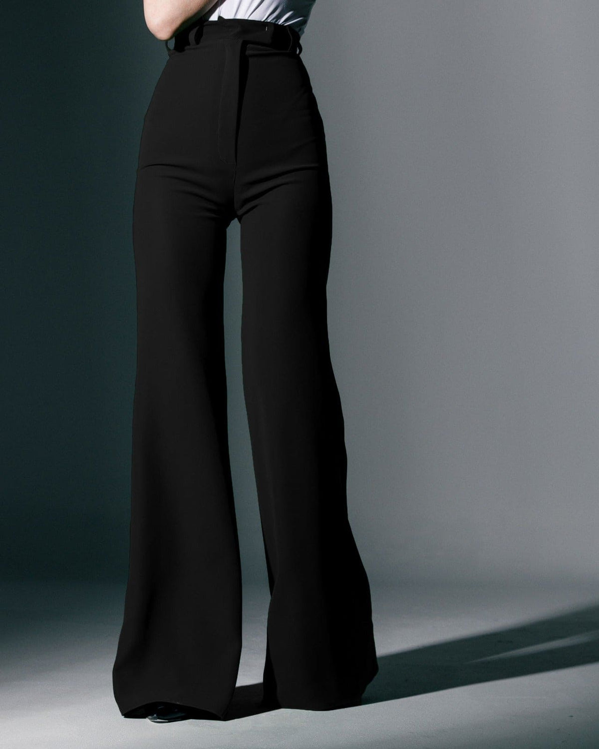 Woman wearing high-waisted black wide-leg trousers and a white tucked-in top
