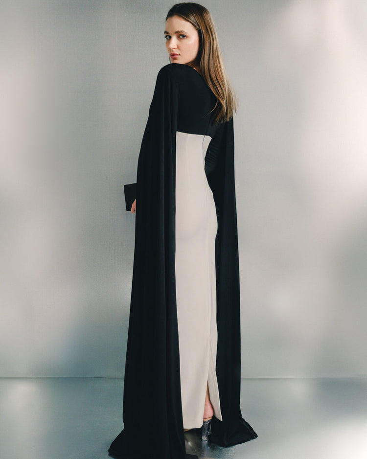 Woman wearing elegant black and white evening dress with dramatic cape sleeves, back view