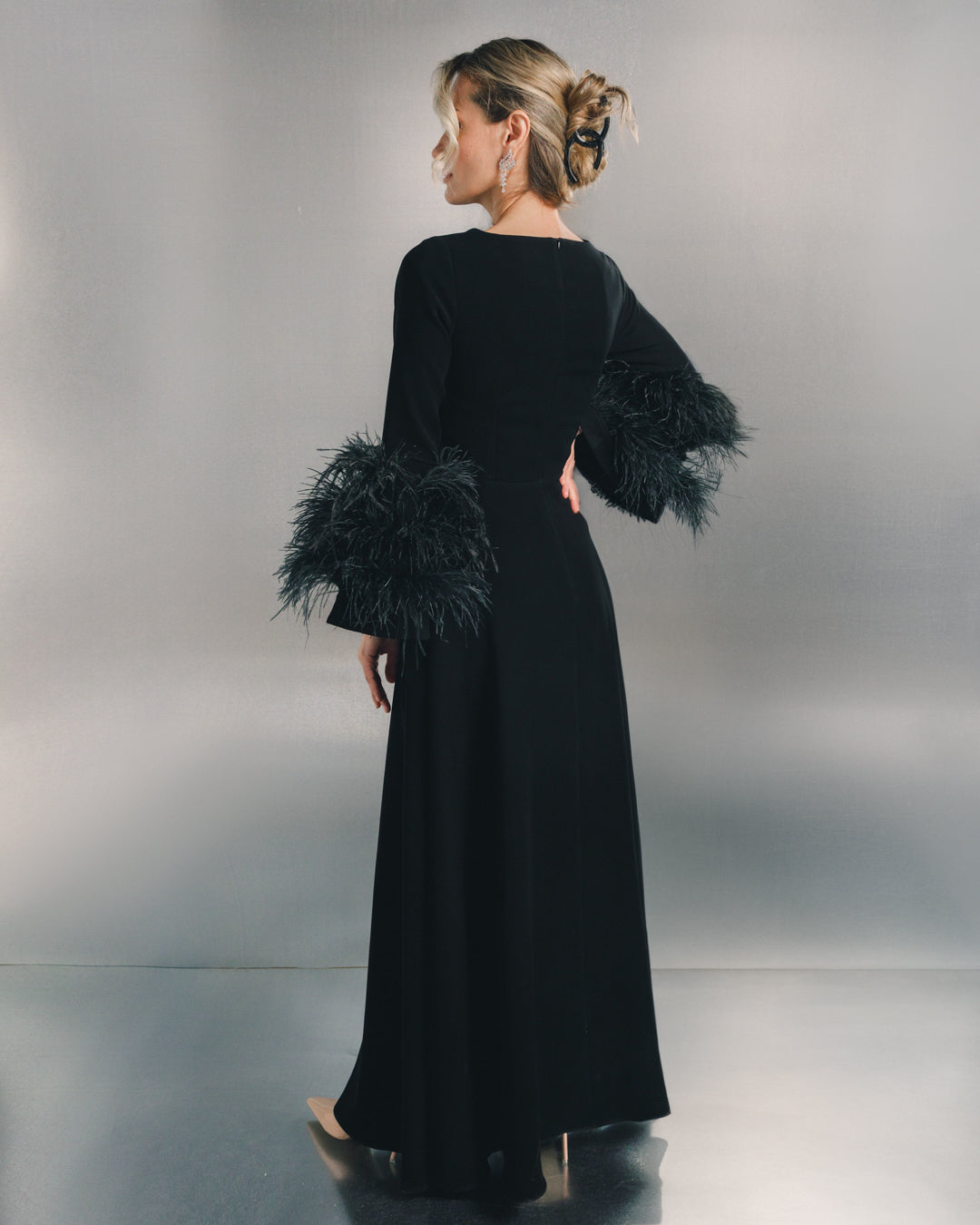 Elegant woman in black long dress with feathered sleeves, metallic background, side view