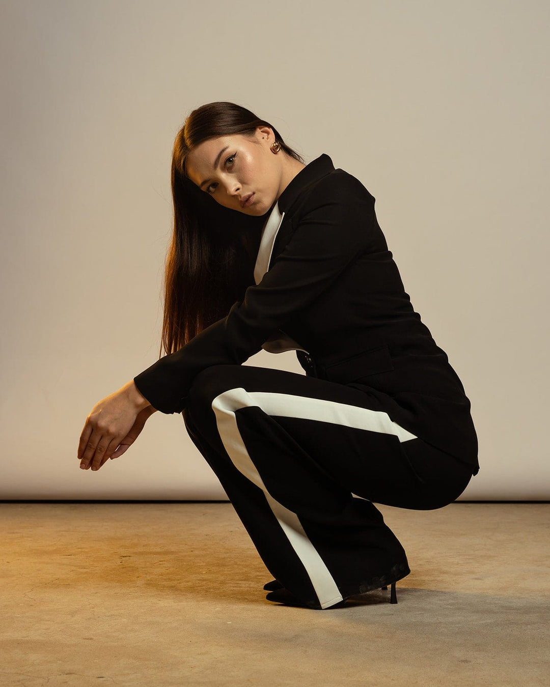 Woman posing in black suit with white stripes and high heels in a studio setting