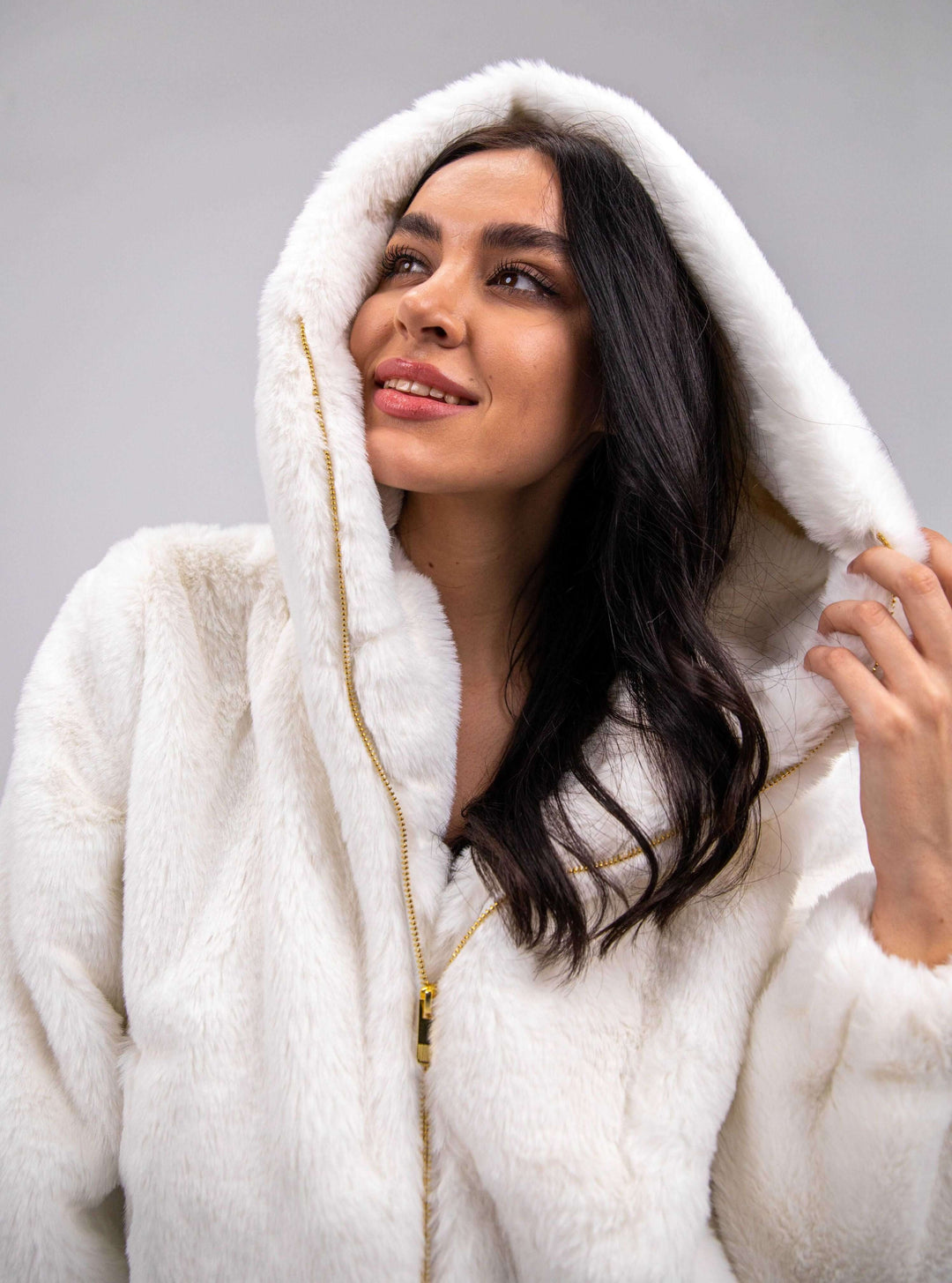Woman wearing a white faux fur hooded jacket with gold zipper, luxury winter fashion