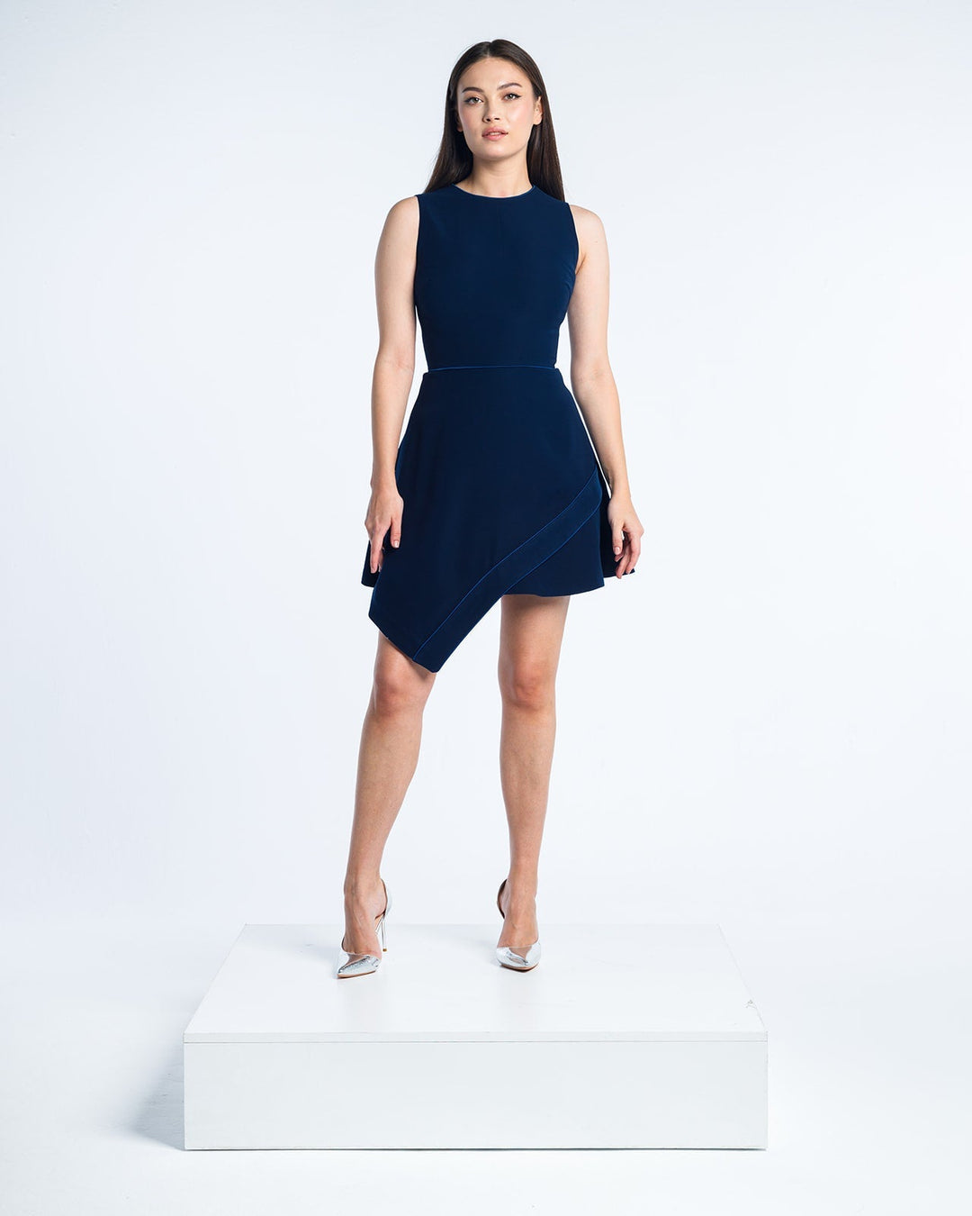 Woman modeling a sleeveless navy blue asymmetric cocktail dress and silver heels