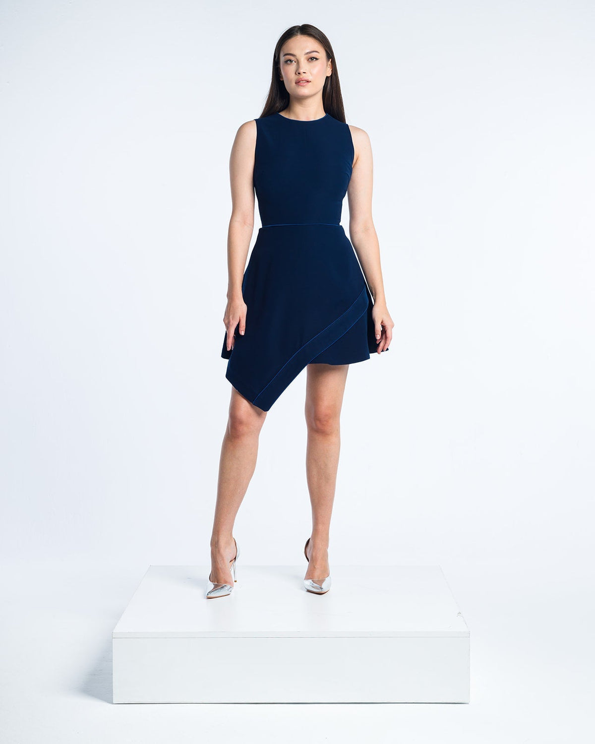 Woman modeling a sleeveless navy blue asymmetric cocktail dress and silver heels