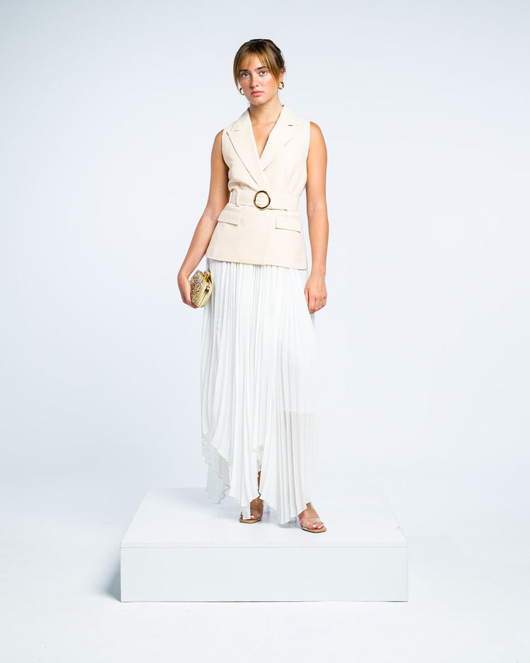 Woman in a sleeveless beige belted blazer and white pleated maxi skirt holding clutch