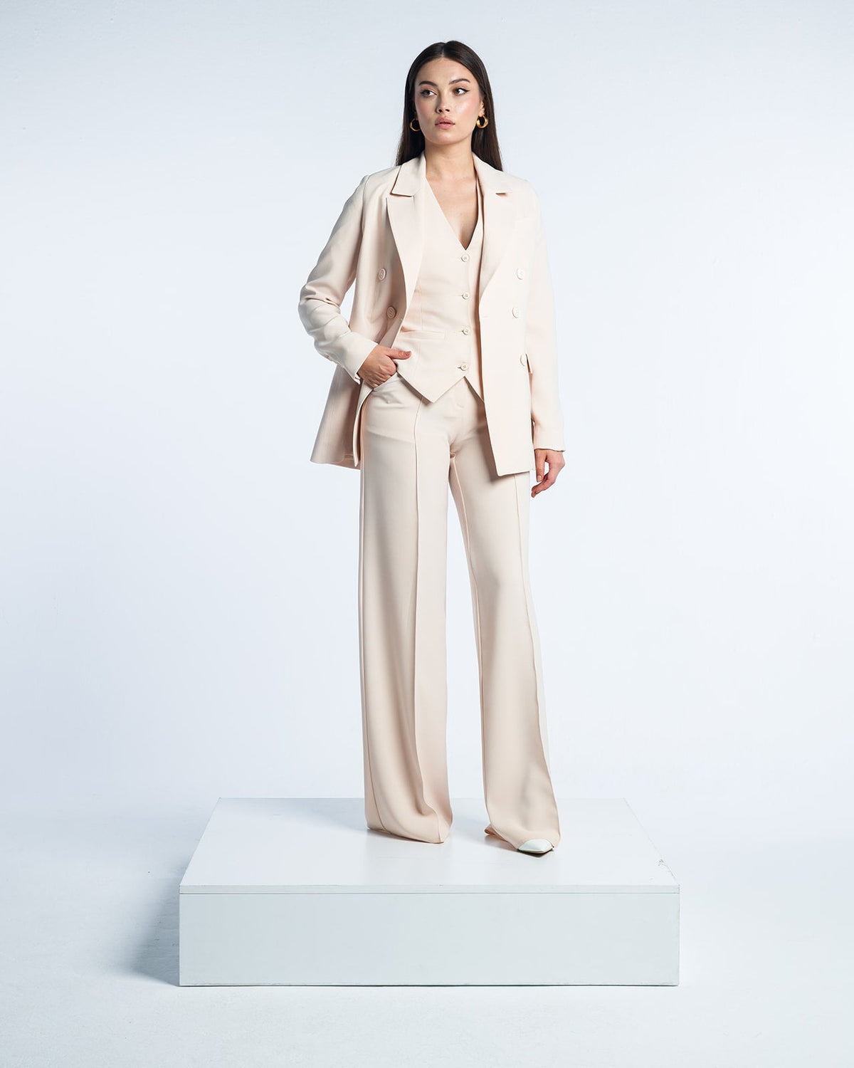 Woman wearing elegant beige suit with blazer, vest, and wide-leg pants on white platform