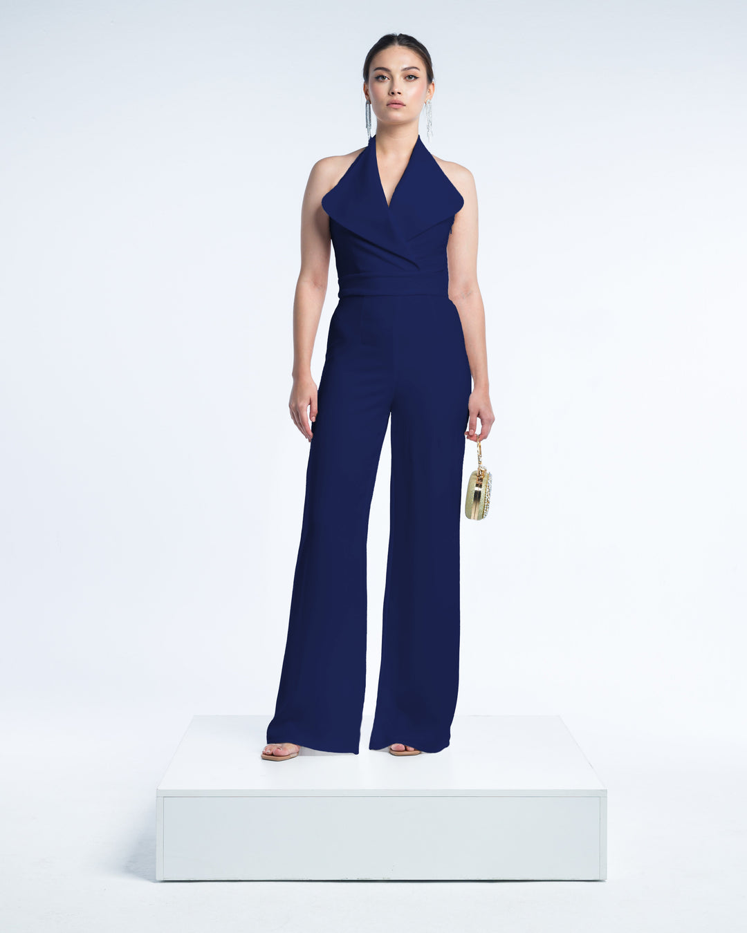 Woman in a dark blue halter neck jumpsuit with wide legs, holding a small clutch