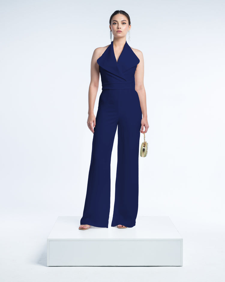 Woman in a dark blue halter neck jumpsuit with wide legs, holding a small clutch