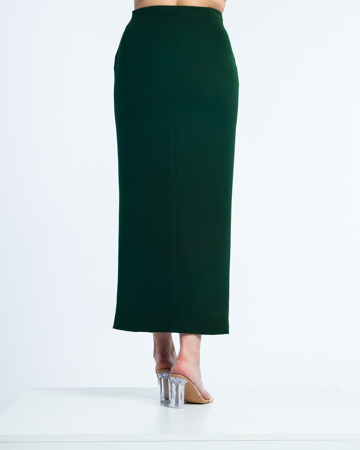 Back view of a woman in a dark green high-waisted maxi skirt and clear heeled sandals