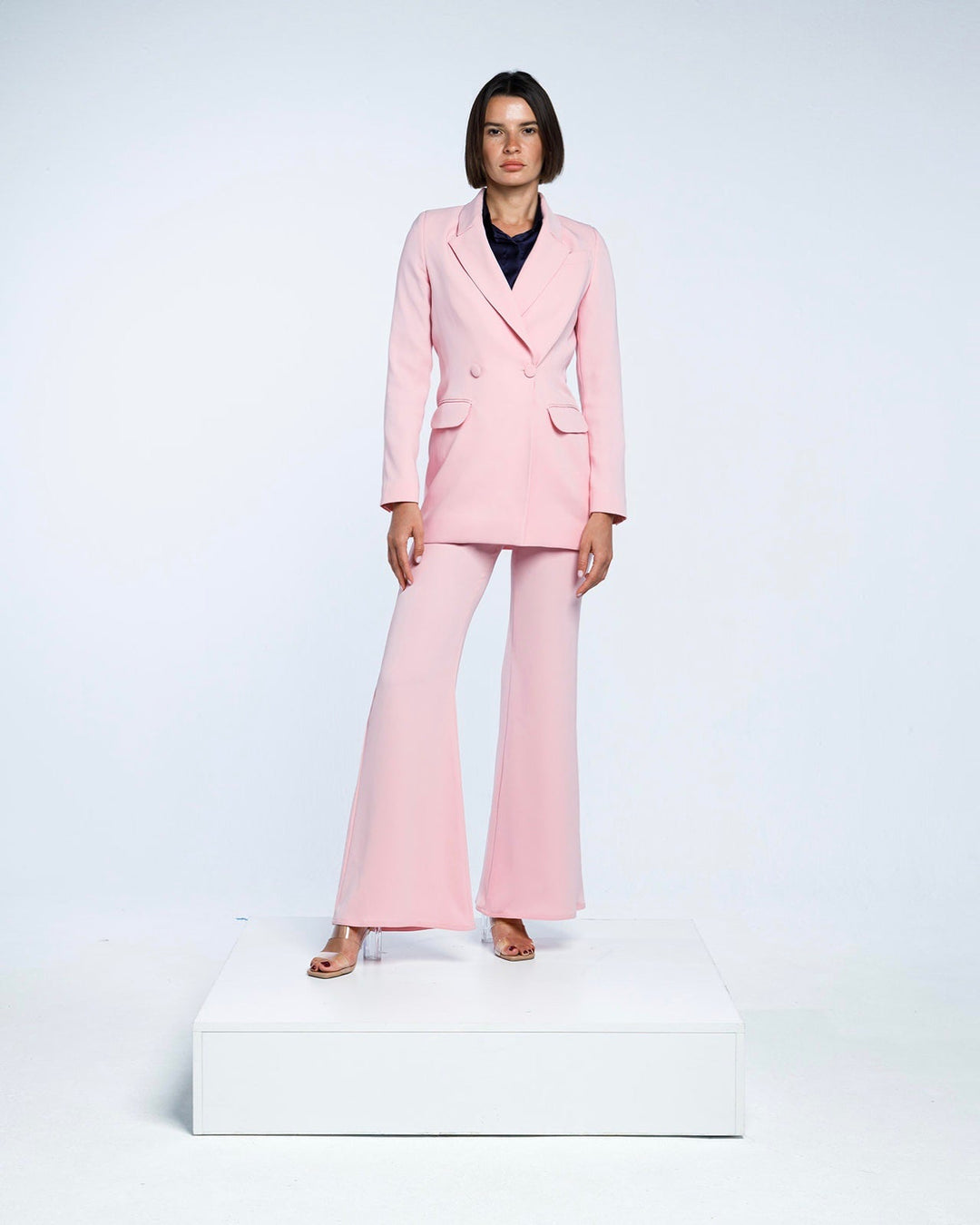 Woman modeling a tailored light pink pantsuit with flared trousers in a studio setting