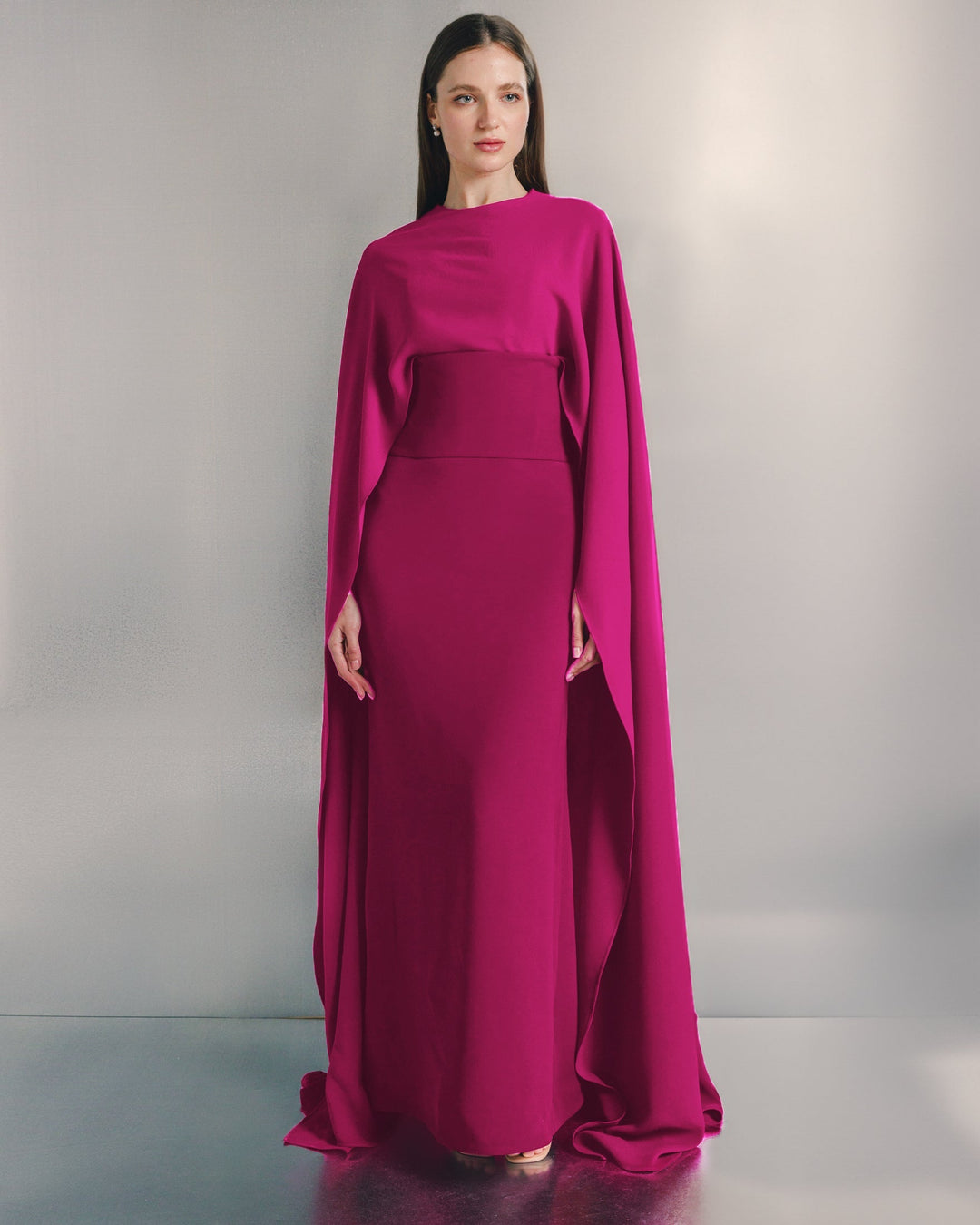 Woman wearing elegant magenta cape gown, floor-length formal dress, minimal background
