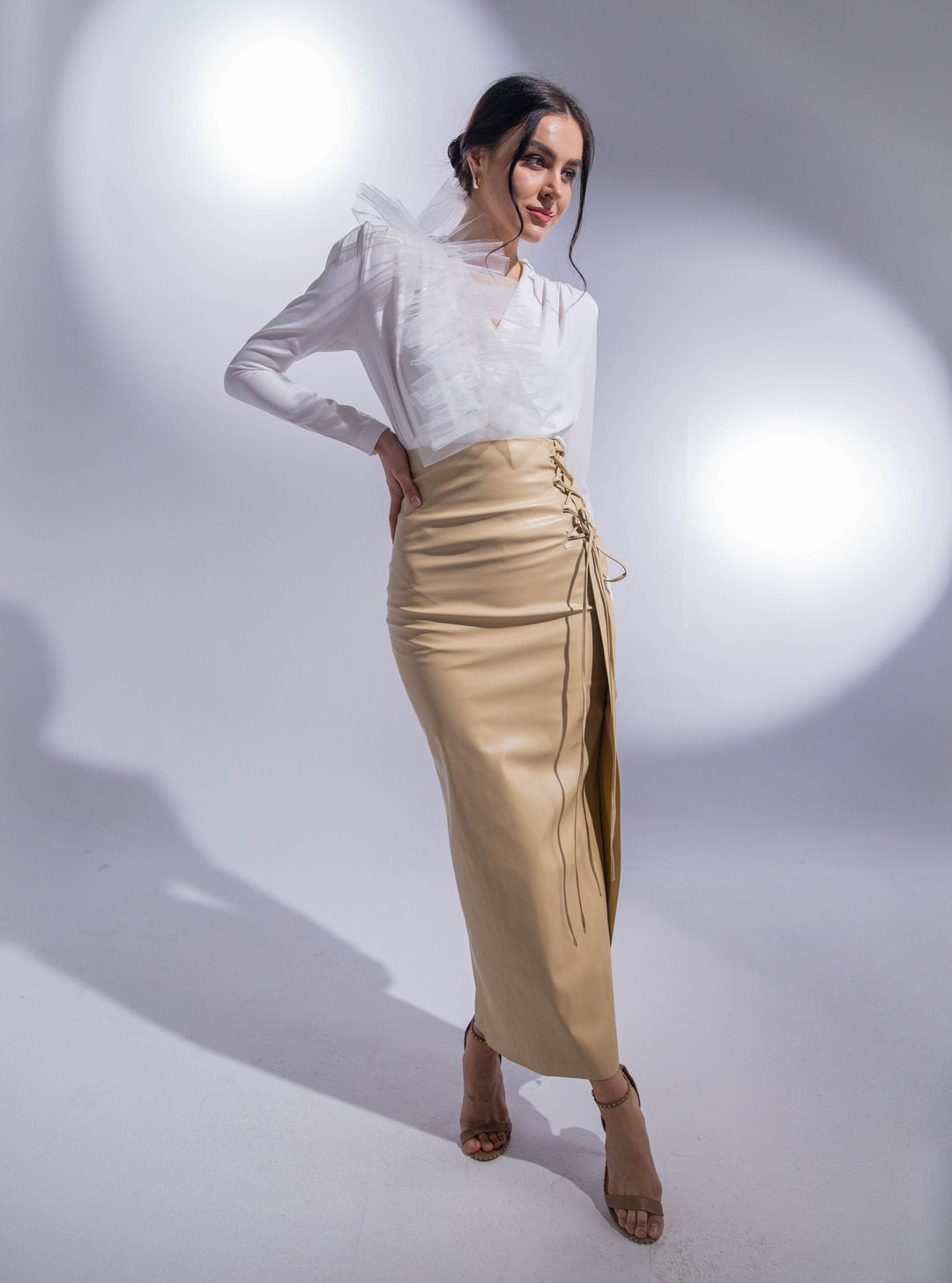 Woman in a beige high-waisted pencil skirt with lace-up detail and a white ruffled blouse
