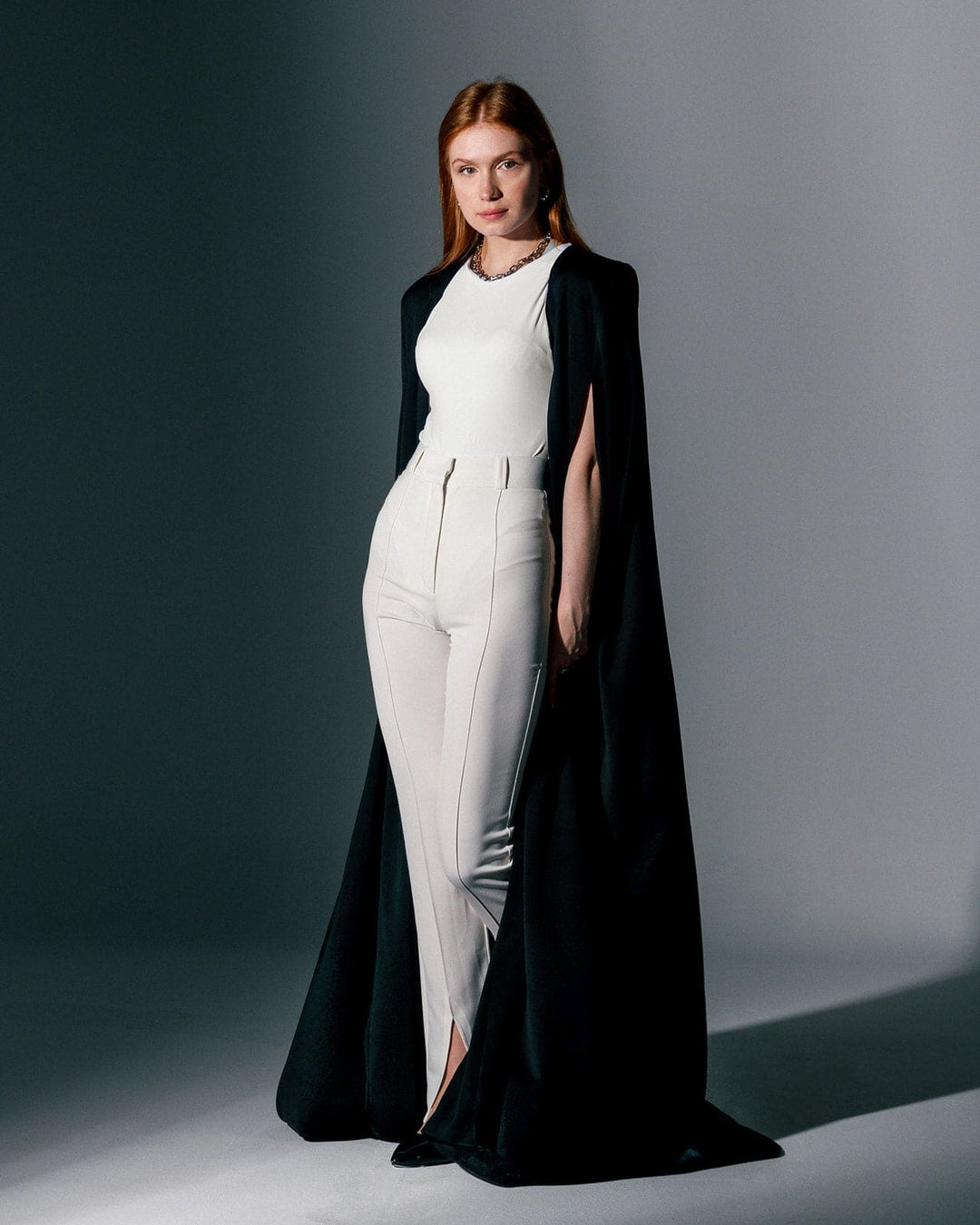 Woman wearing a black crepe cape gown over a white sleeveless jumpsuit, elegant fashion style