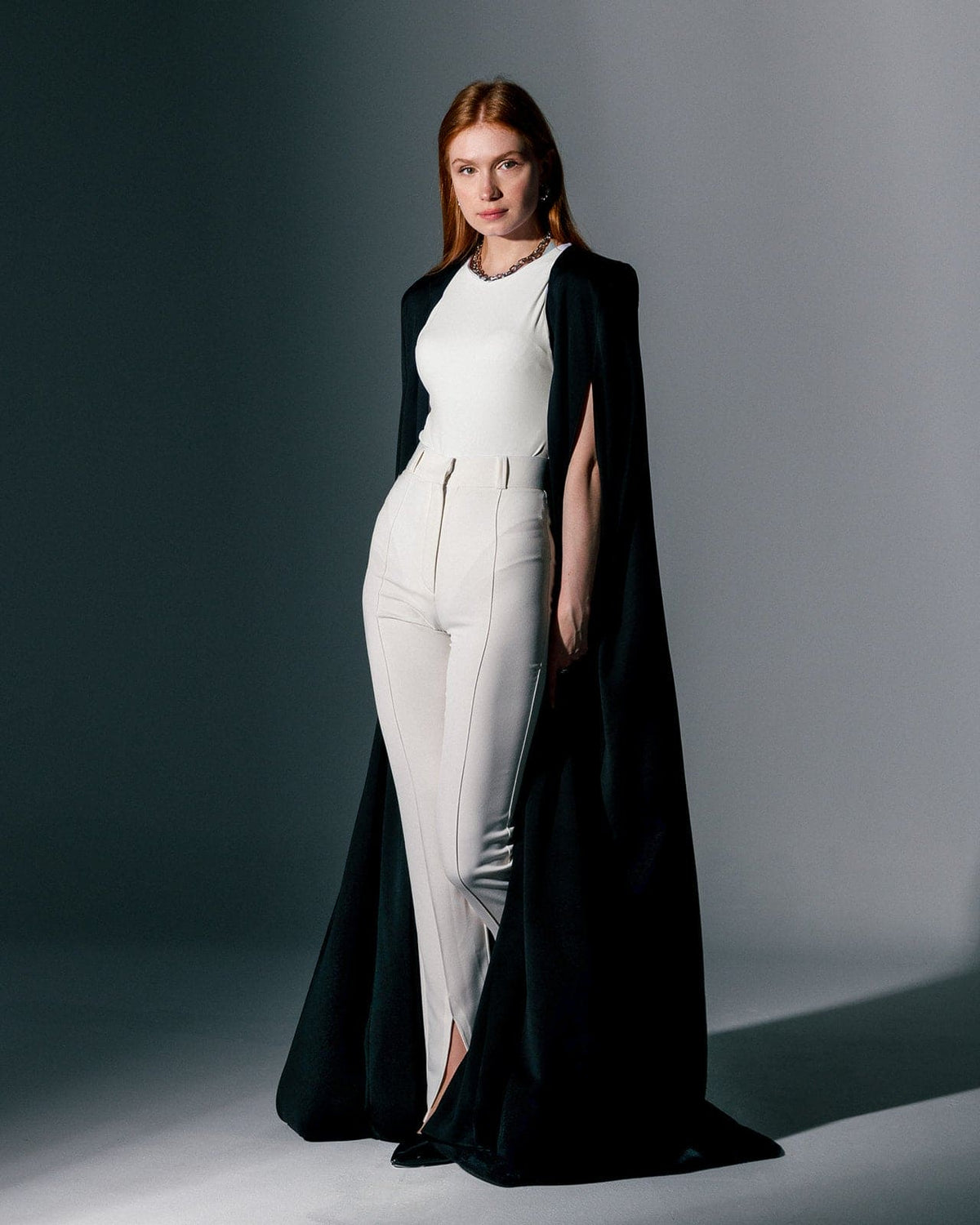 Woman wearing a black crepe cape gown over a white sleeveless jumpsuit, elegant fashion style