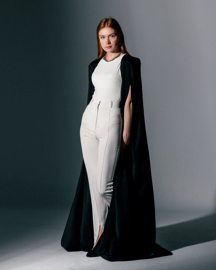 Woman wearing a black crepe cape gown over a white sleeveless jumpsuit, elegant fashion style