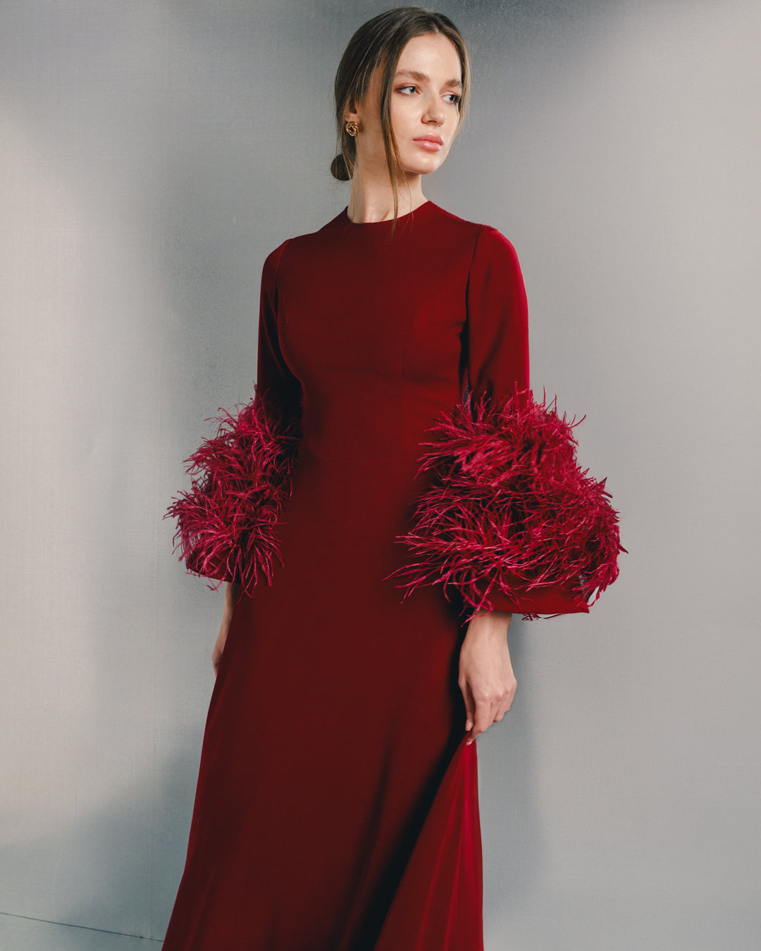 Woman wearing elegant crimson dress with feathered sleeves, premium fashion style