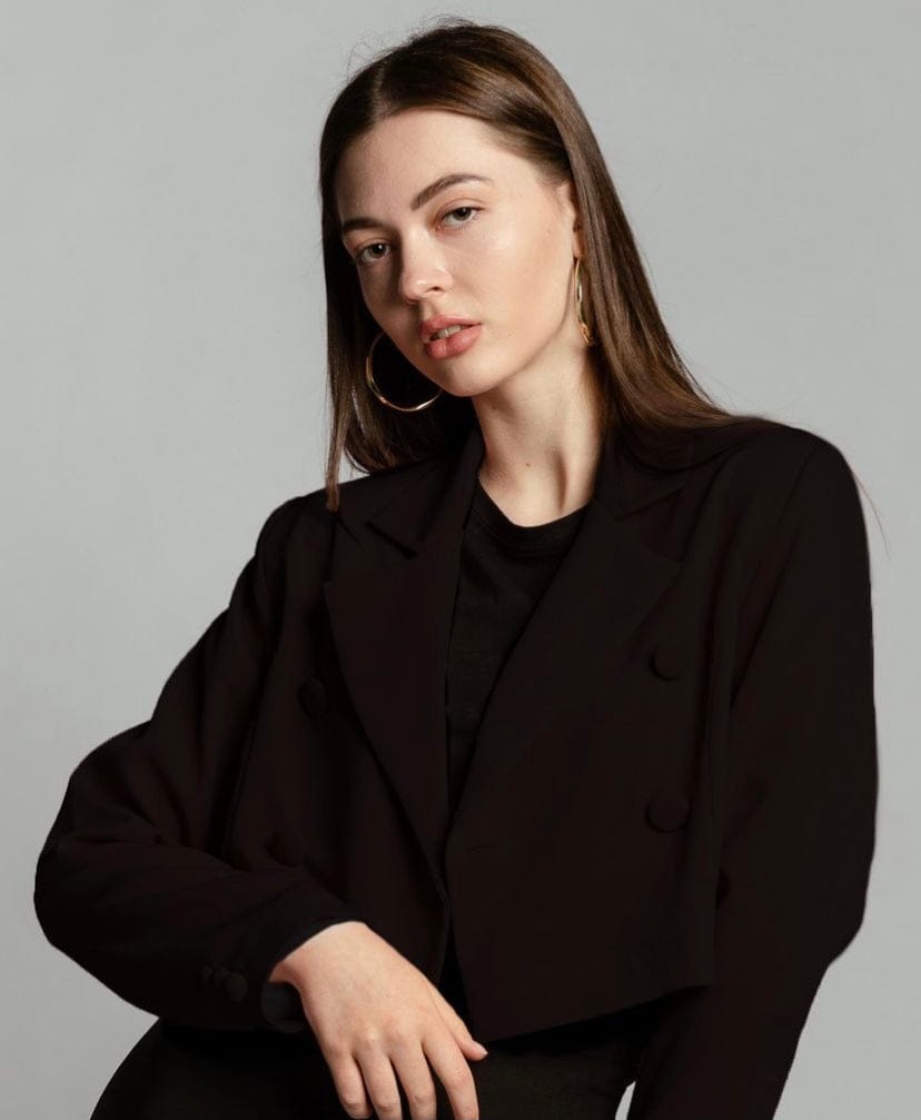 Woman wearing elegant black cropped blazer and hoop earrings against plain background