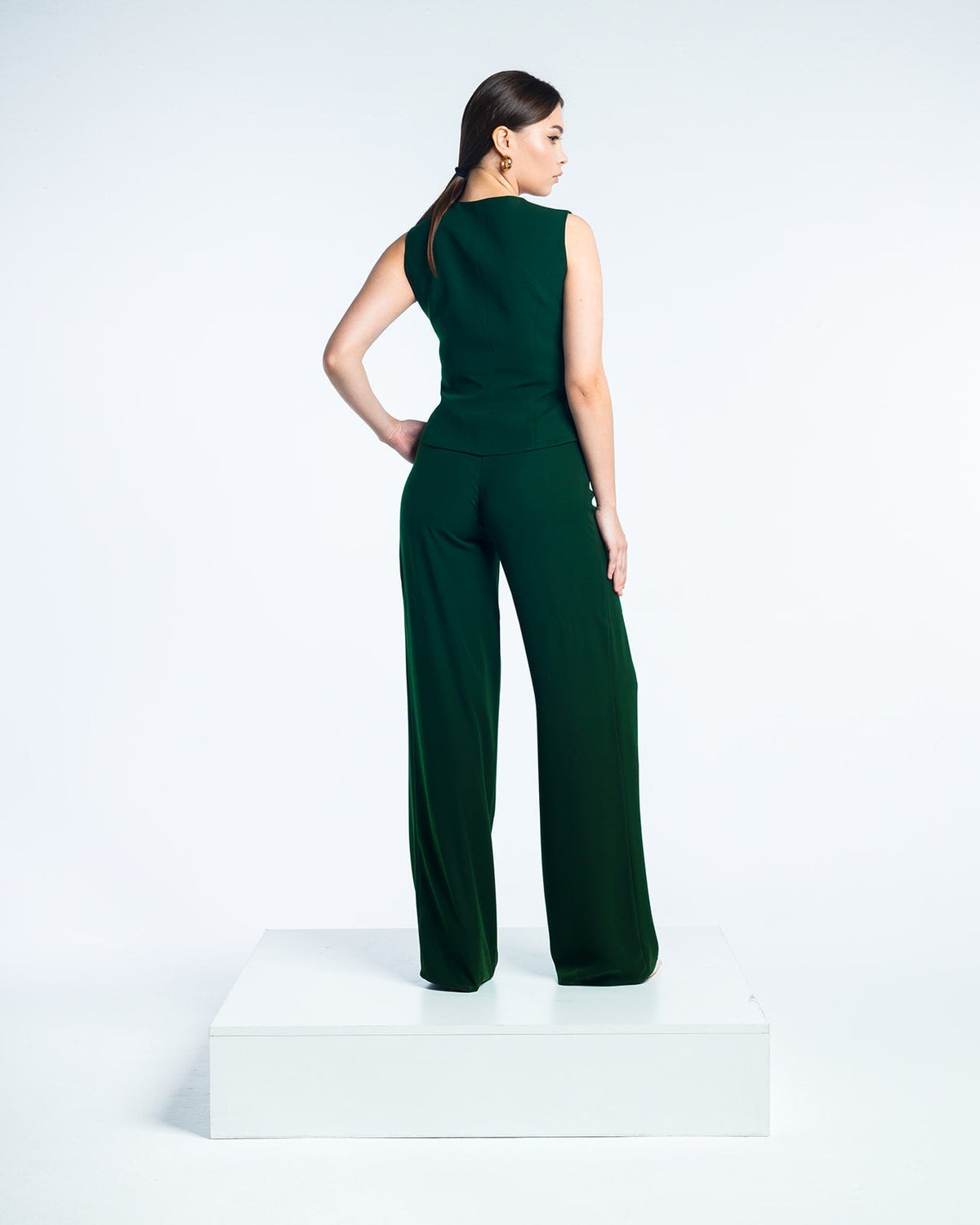 Woman modeling sleeveless dark green jumpsuit with wide-leg pants on white platform