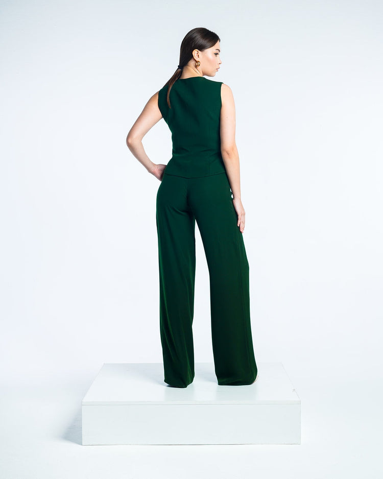 Woman modeling sleeveless dark green jumpsuit with wide-leg pants on white platform