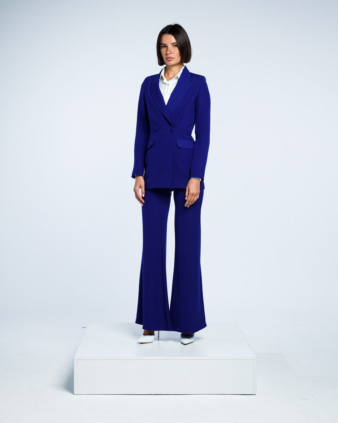 Woman in royal blue tailored pantsuit with flared trousers and white blouse, studio background