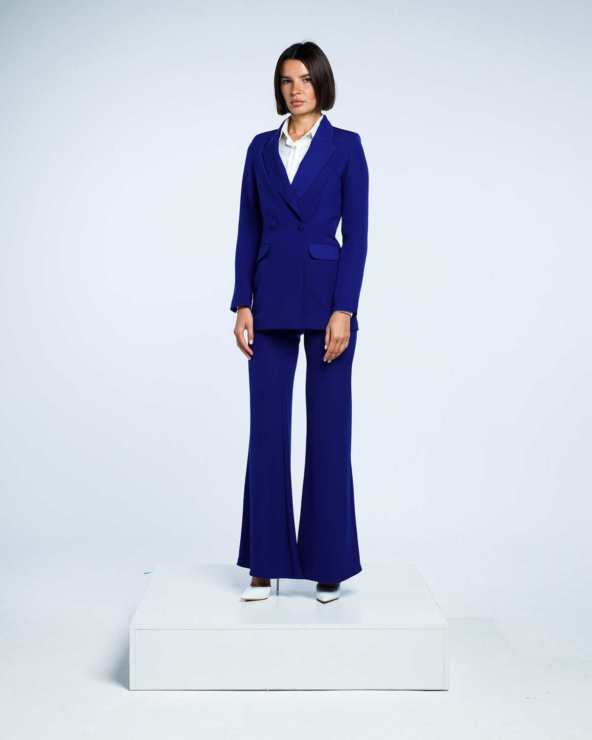 Woman in royal blue tailored pantsuit with flared trousers and white blouse, studio background