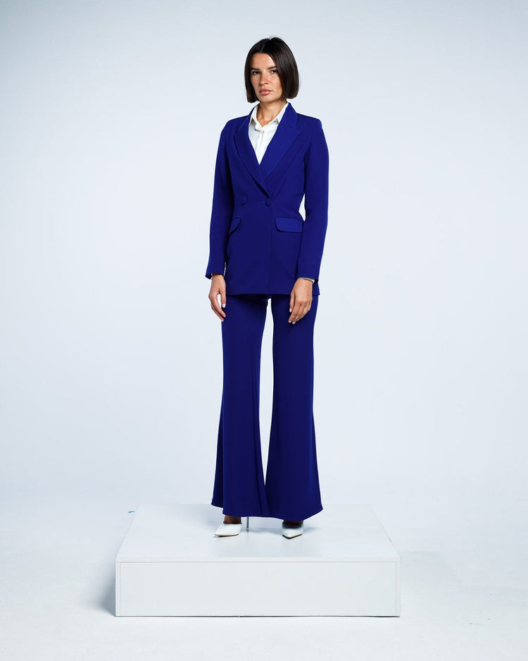 Woman in royal blue tailored pantsuit with flared trousers and white blouse, studio background