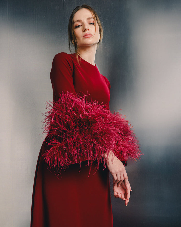 Woman in elegant red dress with dramatic feathered sleeves, luxury fashion style