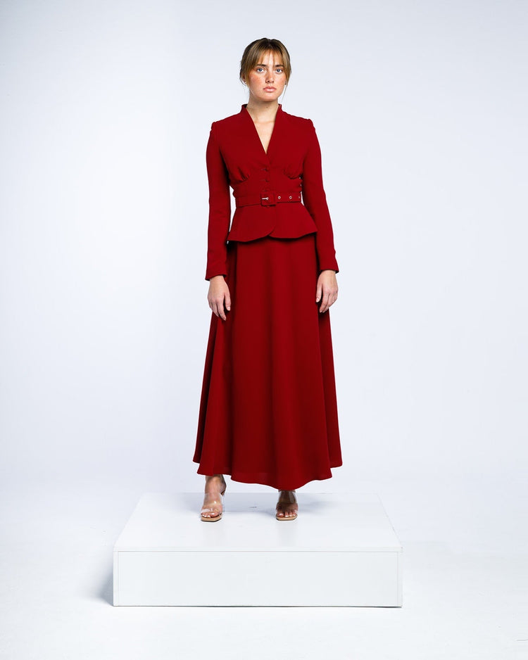 Woman in an elegant long-sleeve red belted maxi dress with a v-neck standing on a white platform