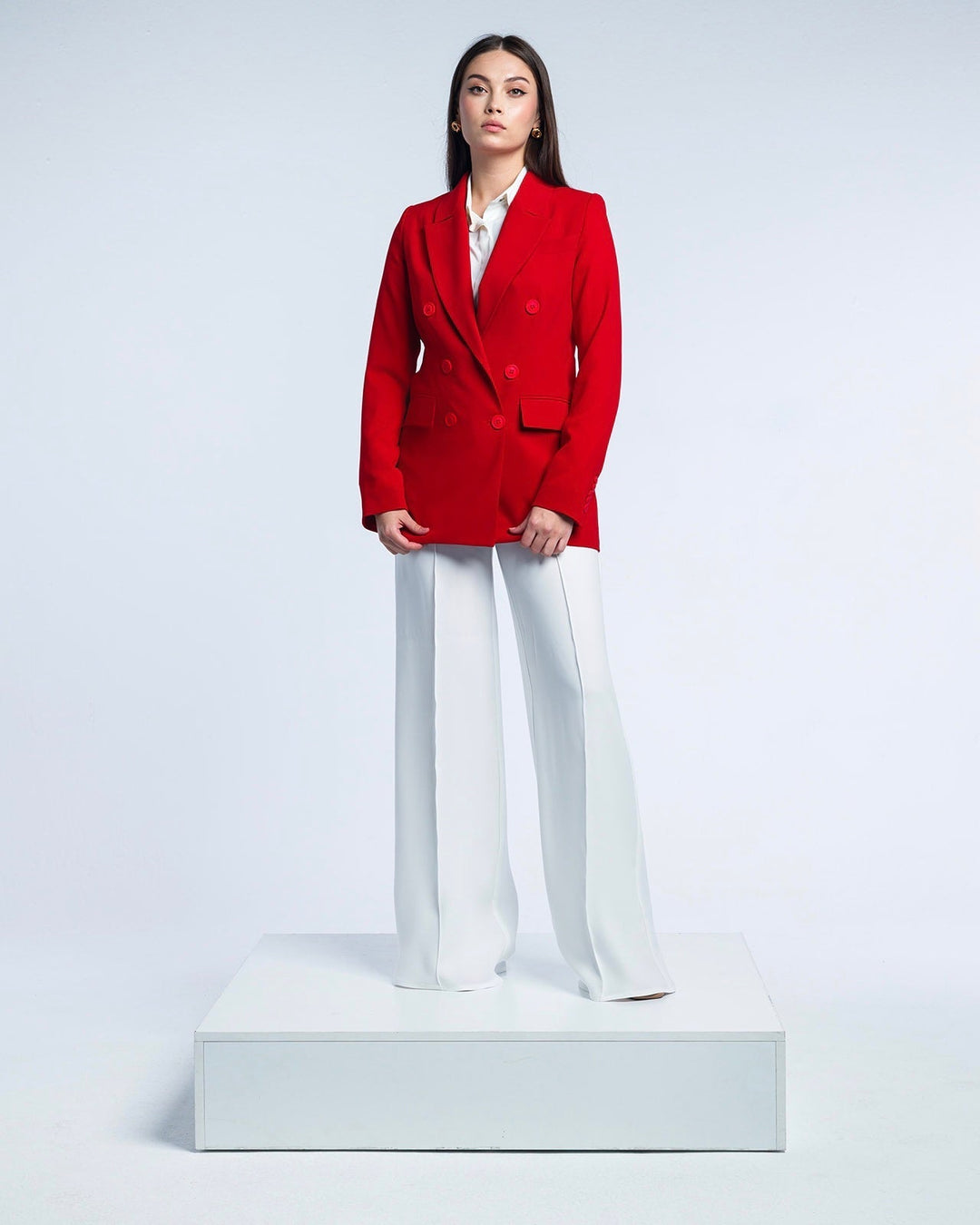 Woman wearing red double-breasted blazer and white wide-leg pants in studio setting