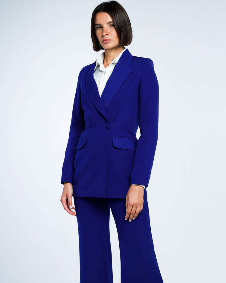 Woman wearing royal blue tailored pantsuit with white blouse against plain background