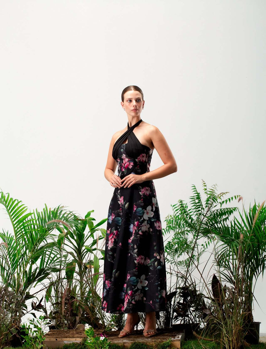 Woman in a black floral halter dress standing among lush green plants, elegant fashion look