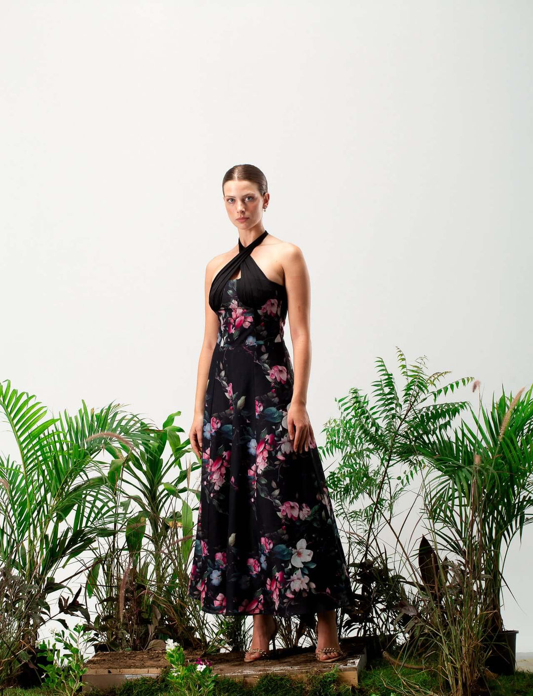 Woman in black floral halter neck maxi dress standing among green plants