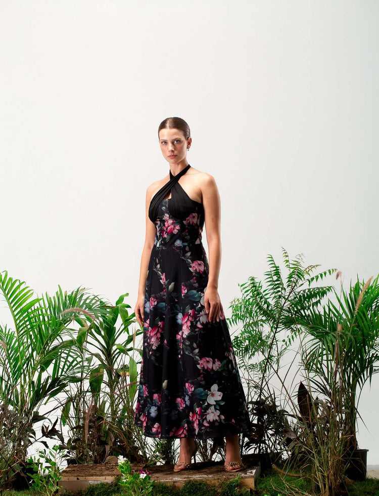Woman in black floral halter neck maxi dress standing among green plants