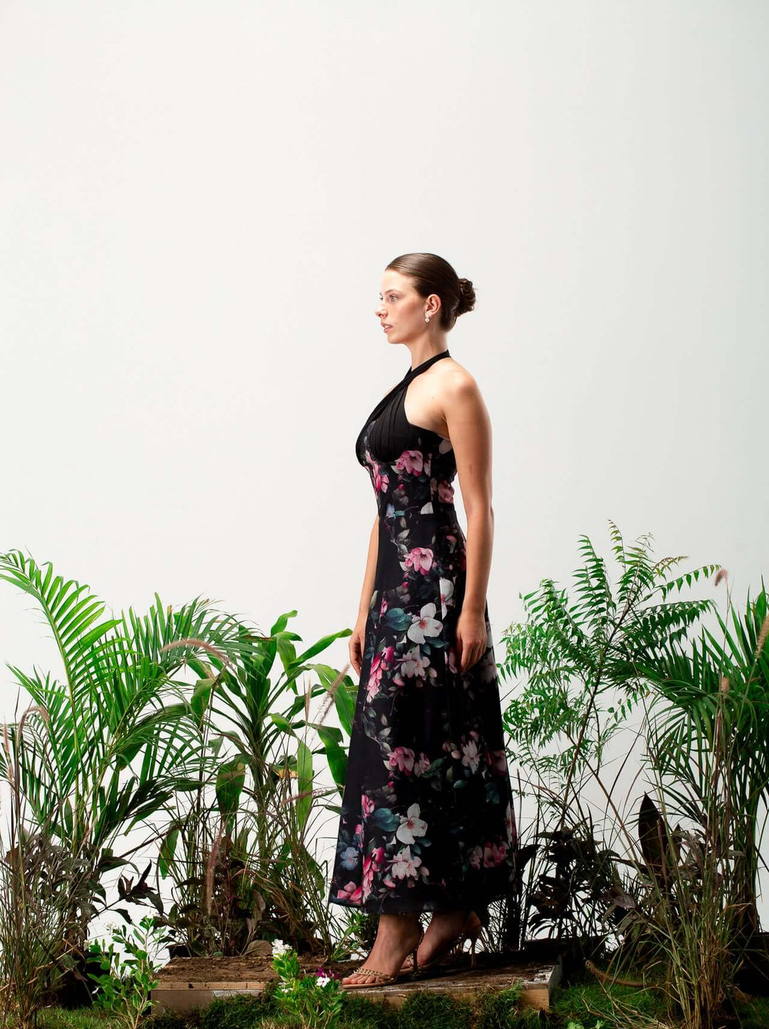 Woman in a sleeveless black floral maxi dress standing among green tropical plants