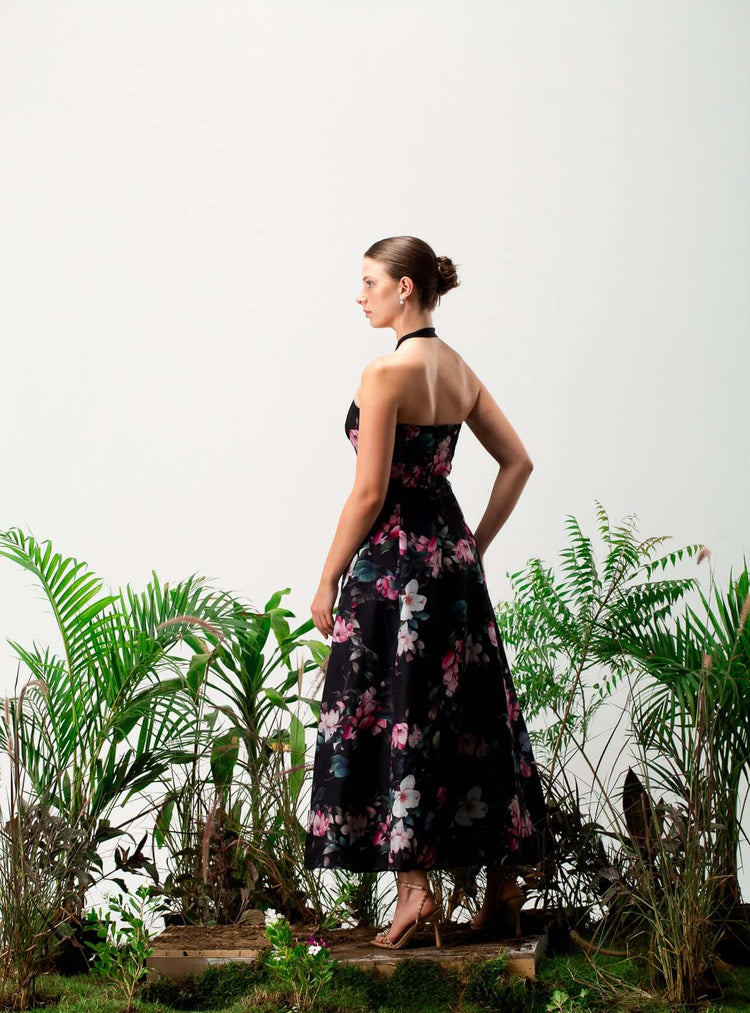 Woman in a black floral halter dress standing among green plants, side view